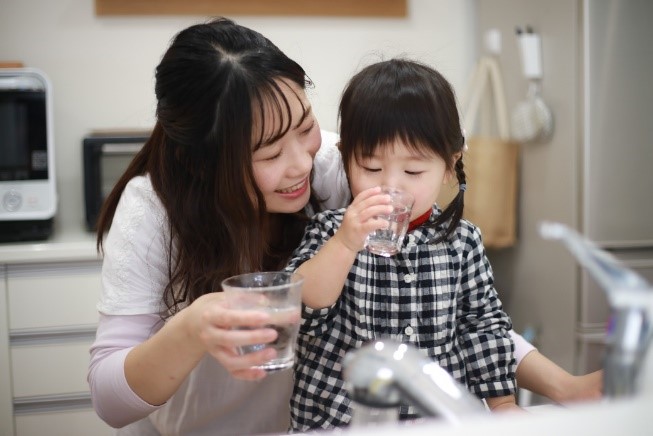 mother and daughter filling up glass of water at the sink