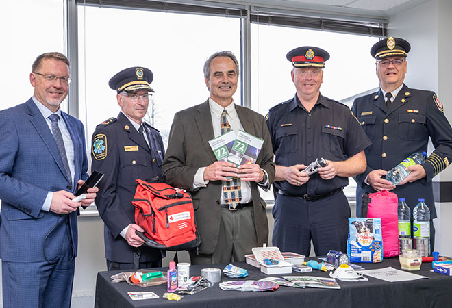 5 persons standing behind a table with various emergency kit items on it.